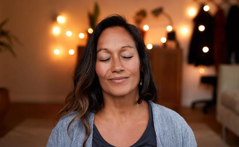 Frau lächelt entspannt in dunklem Meditationsraum